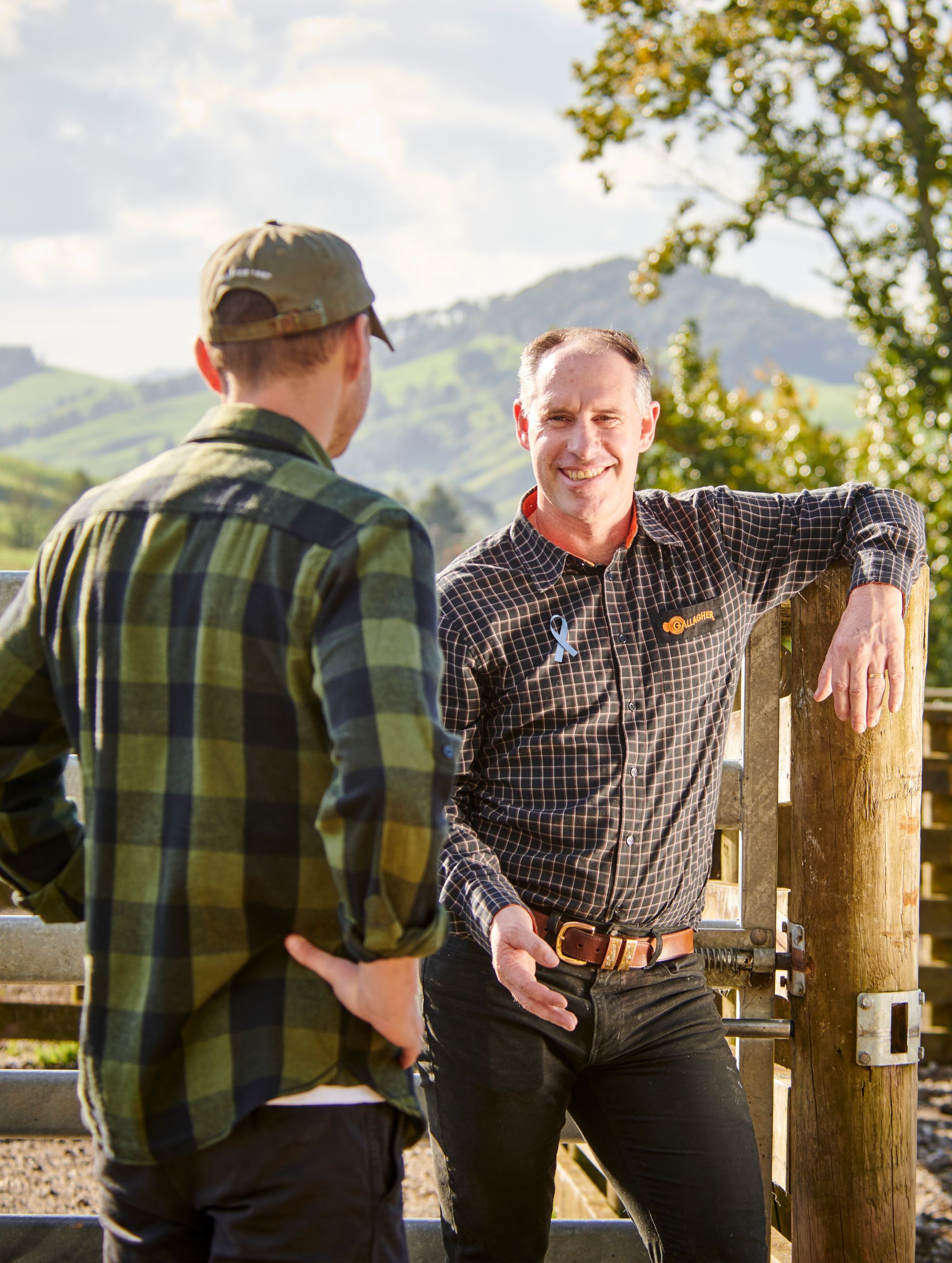 Un miembro del equipo Gallagher hablando con un granjero, lleva una cinta azul prendida en el pecho para promover Movember.
